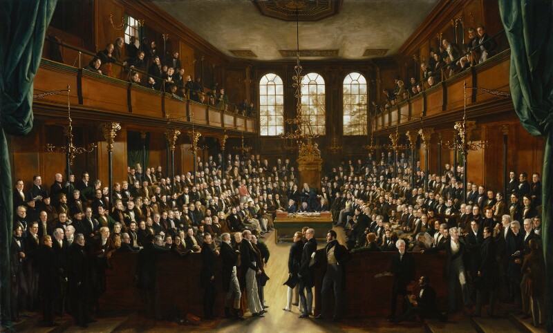 A coloured painting of the House of Commons chamber before the fire of 1834. looking into the chamber, in the middle at the back is the ornate golden speakers chair, with the Table of the House in front of it, each side, the chamber is full of MPs sitting on four rows of benches either side, there are also people standing behind and around the side. Above each side is a viewing gallery also full of people overlooking the chamber. The chamber walls a wooden with a dark golden brown polish, with black and gold detailed post holding up the galleries. There is a golden chandelier hanging low over the Table of the House, and behind the speaker is a set of three tall slim windows.