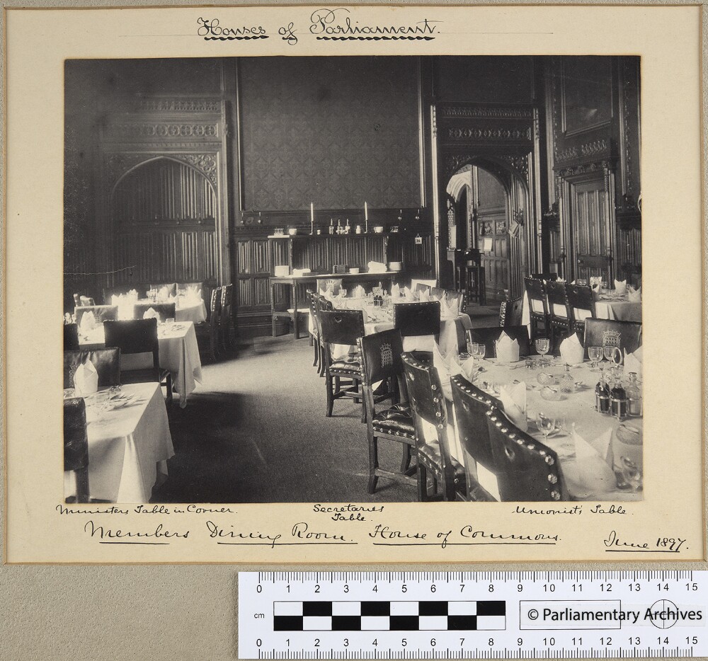 A photograph of a dining room. There are multiple tables covered in white table cloths and serveware. The chairs are studded.