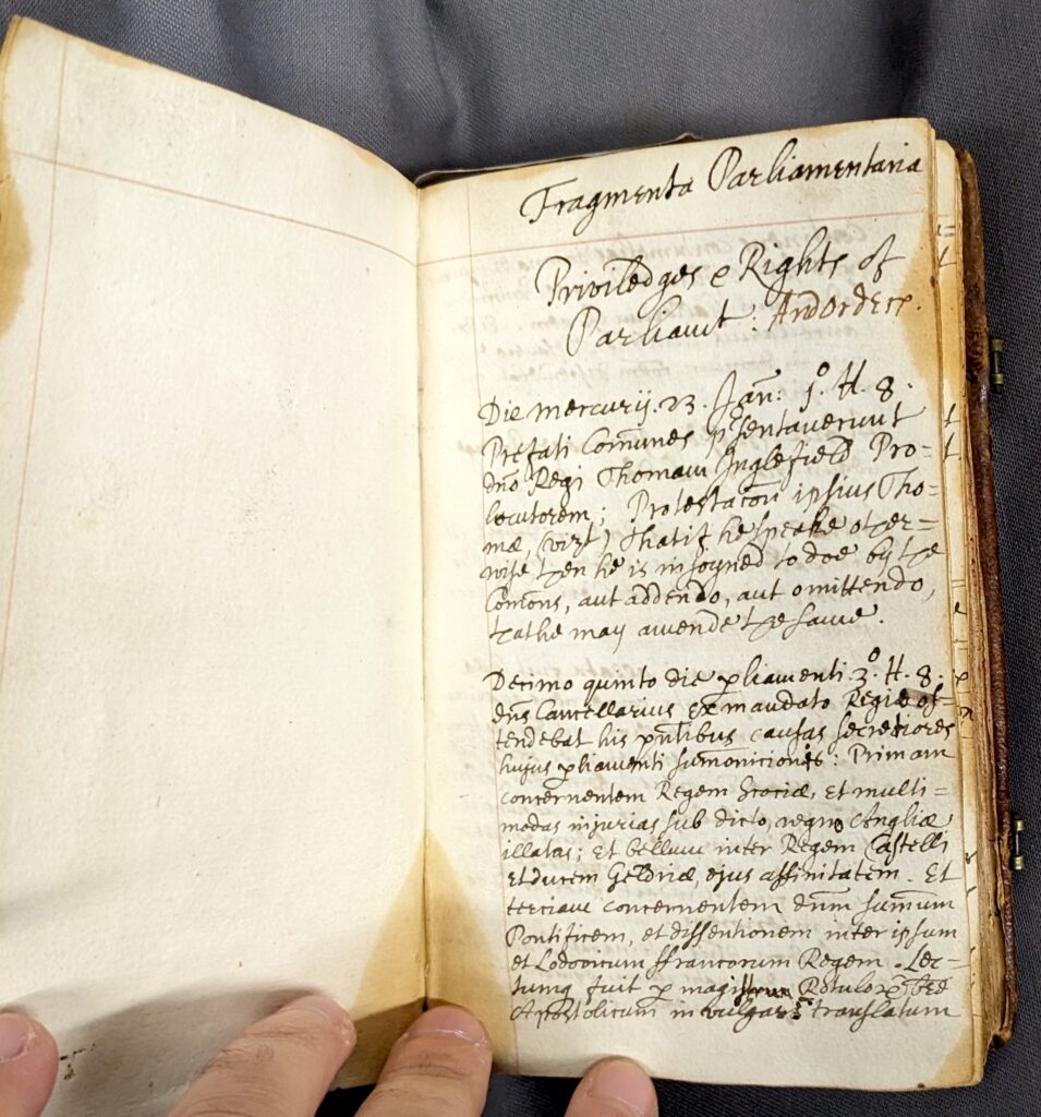A coloured photograph a manuscript page of handwritten text in Latin, the page is a faded yellow colour. The writing is illegible, but is the title page of the Clerk of Parliaments' 'Fragmenta Parliamentaria'.